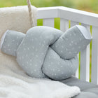 Die Wickeltischrolle Musselin grau Pusteblumen von KraftKids GmbH mit weißem Pusteblumenmuster liegt auf einer kuscheligen cremefarbenen Decke und einem grauen Kissen in einem weißen Kinderbett, im Hintergrund ist Grün zu sehen.