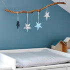 Eine minimalistische Wickelstation mit einem KraftKids Wickelaufsatz weiß für eine 160 cm HEMNES Kommode, gepolsterter Unterlage, Holzhäusern, gestapelten Windeln und einem handgefertigten Sternenmobile an einer beruhigenden blauen Wand.