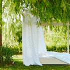 Ein Holzbett mit weißer KraftKids Bettwäsche und der Bettbaldachin Musselin gelbe Zitronen von KraftKids steht auf grünem Rasen, teilweise beschattet von belaubten Ästen inmitten üppigen Grüns.