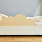 Ein Kinderbett mit hellem Holzrahmen bietet der KraftKids Rausfallschutz aus Leimholz Wolke. Cremefarbene Blumenbettwäsche, hellgraue Wände und ein Holzfußboden schaffen einen gemütlichen, kindersicherer Fallschutz-Schlafraum.