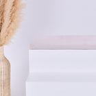 Eine große geflochtene Vase mit Pampasgras steht neben einem minimalistischen weißen Stufenpodest, gekrönt von der KraftKids GmbH Sitzauflage für Ikea TROFAST Cord Breitcord Beige Taupe, vor einem schlichten hellen Hintergrund.