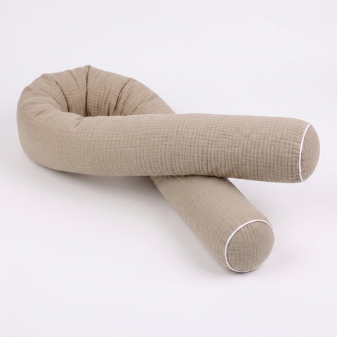 Die KraftKids GmbH Wickeltischrolle Musselin beige, mit strukturiertem Stoff und weißer Paspel an beiden Enden, ist in geschwungener, gekreuzter Position auf weißem Grund abgebildet.