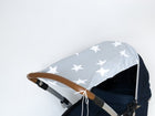 Der KraftKids Sonnensegel große weiße Sterne auf Grau, abgebildet auf einem Kinderwagen mit braunem Griff und grauem Verdeck mit großen weißen Sternen, bietet atmungsaktiven Baumwollsonnenschutz für Babys vor einem schlichten weißen Hintergrund.