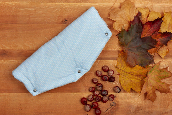Eine blaue, handgenähte Stoffwindel mit Druckknöpfen ruht auf Holz, umgeben von Herbstblättern und Kastanien. Der weiche Fleece ist besonders kuschelig - ideal, um ihn an kühlen Tagen mit dem KraftKids Kinderwagenmuff kleine Blätter hellblau auf Weiß zu kombinieren.