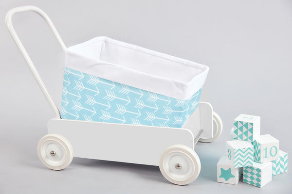 Ein weißer Spielzeugwagen mit dem KraftKids Körbchen weiße Pfeile auf Blau, einem handgenähten blauen Baumwollkorb mit weißen Pfeilen, steht neben pastellblauen und weißen Dekoblöcken auf hellgrauem Hintergrund. Ideal für die Aufbewahrung auf dem Wickeltisch.