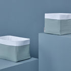 Zwei rechteckige KraftKids Körbchen Musselin mint mit hellblauen Seiten und weißen Oberseiten, ideal für die Aufbewahrung auf einem Wickeltisch, werden auf blauen Plattformen vor einem passenden blauen Hintergrund präsentiert.