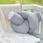 Ein KraftKids Wickeltischumrandung Musselin grau Punkte liegt auf einem weißen Kinderbett mit grauen Polstern und Latten, neben einer weichen cremefarbenen Decke, mit einem verschwommenen grünen Hintergrund, der von außen sichtbar ist.