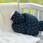 Ein KraftKids Wickeltischumrandung Musselin dunkelblauer Anker mit weißem Ankermuster ruht auf einer cremefarbenen Fleecedecke auf einer Outdoor-Bank, umgeben von sanft verschwommenem Grün.