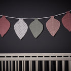 Ein weißes Kinderbett steht an einer dunklen Wand, über der die KraftKids Wimpelkette Musselin in rosa mint mit grauen Punkten auf Weiß hängt - eine bezaubernde pastellfarbene Girlande, die eine schöne Idee für die Kinderzimmerdekoration ist.