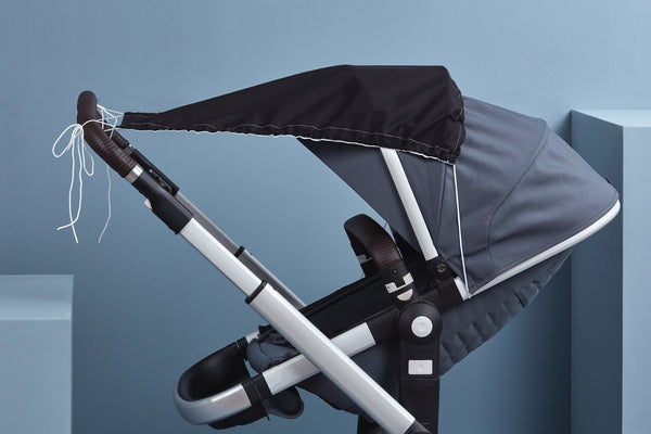 Der KraftKids Sonnensegel Unischwarz ist ein modernes Kinderwagenverdeck in Schwarz und Grau, im Profil auf hellblauem Hintergrund, mit weißen Schnüren und bietet optimalen Sonnenschutz für Ihr Baby.