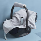 Eine KraftKids Babydecke für Babyschale in grauem Musselin mit Pusteblumenmuster bedeckt eine Babyschale und den Griff, präsentiert auf einer hellblauen Oberfläche vor passendem Hintergrund.