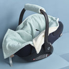 Eine mintfarbene "Decke für Babyschale Winter Musselin mint Pusteblumen" von KraftKids steht auf einem blauen Podest mit gepolstertem Bezug, Griff und grauen Sicherheitsgurten, die einen weichen, gemütlichen Look vor blauem Hintergrund schaffen.