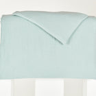 Ein Bettwäscheset Musselin mit goldenen Punkten auf Grün von KraftKids, ordentlich gefaltet und über einen weißen rechteckigen Block auf schlichtem weißem Hintergrund drapiert.