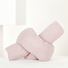 Die KraftKids Wickeltischumrandung Musselin mit goldenen Punkten auf Rosa, weich und in Knotenform, liegt auf weißem Untergrund mit minimalistischen weißen geometrischen Formen im Hintergrund.