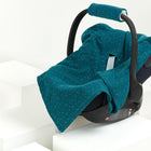 Eine KraftKids Babydecke für Babyschale Sommer aus Musselin mit goldenen Punkten auf petrol überzieht eine schwarze Babyschale, die auf weißen geometrischen Blöcken vor neutralem Hintergrund präsentiert wird.