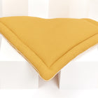 Die Wickelauflage Waffel Piqué senf von KraftKids, ein V-förmiges Kissen aus strukturiertem senfgelbem Stoff, sitzt auf weißen geometrischen Blöcken - eine ideale, stilvolle Ergänzung für das Kinderzimmer Ihres Babys.