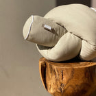 Ein KraftKids Wickeltischumrandung Leinen Natur Braun ruht auf einem Holzhocker mit einer strukturierten Oberfläche. Das Sonnenlicht wirft Schatten auf die Wand und das Produkt und hebt den weichen Leinenstoff und das einzigartige, geknüpfte Design hervor.