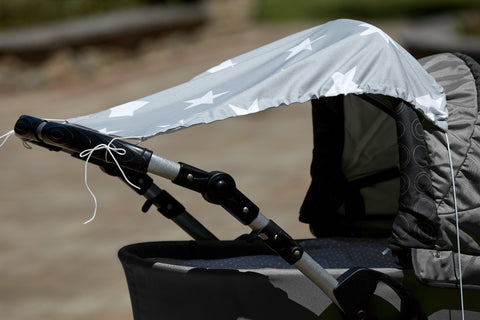 Eine Nahaufnahme eines grauen Kinderwagens mit dem KraftKids Sonnensegel große weiße Sterne auf Grau für optimalen Sonnenschutz, draußen im Sonnenlicht mit sichtbarer loser weißer Schnur.