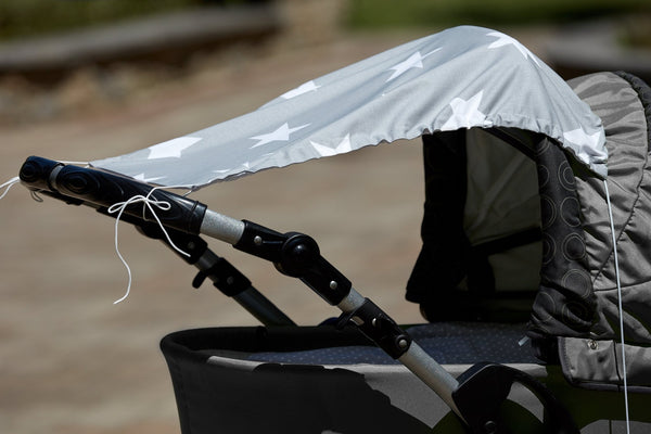 Eine Nahaufnahme eines grauen Kinderwagens mit dem KraftKids Sonnensegel große weiße Sterne auf Grau für optimalen Sonnenschutz, draußen im Sonnenlicht mit sichtbarer loser weißer Schnur.