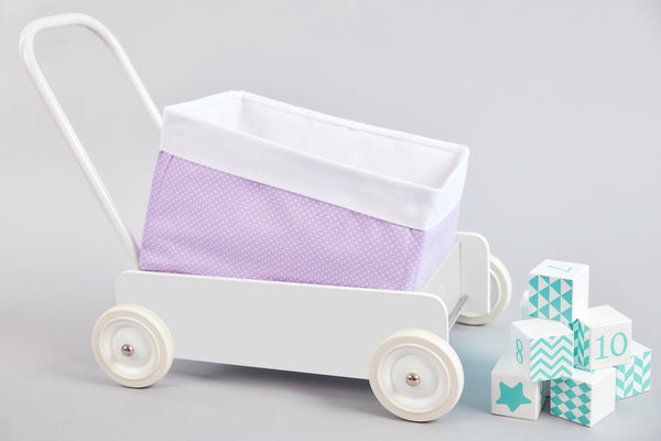 Ein weißer Spielzeugwagen mit dem KraftKids Körbchen Uniweiss weiße Punkte auf Lila sitzt neben blauen und weißen Deko-Blöcken und bietet stilvolle Aufbewahrung im Kinderzimmer vor einem hellgrauen Hintergrund.