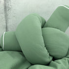 Eine Nahaufnahme des KraftKids Wickeltischumrandung Doppelkrepp Grün Jade, ein zartes grünes Kissen mit weißer Paspel, geformt wie ein großer Knoten und vor einem hellgrauen Hintergrund.