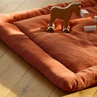 Eine gemütliche KraftKids Krabbeldecke Doppelkrepp Rot Herbstrot liegt auf einem Holzboden, auf dem ein Holzspielzeugpferd auf Rädern und kleine Bauklötze verstreut sind, während das Sonnenlicht die einladende Szene erhellt.