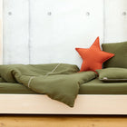 Das KraftKids Bettwäscheset Doppelkrepp Grün Herbstgrün aus 100% Baumwolle mit einem passenden Kissen und einem orangefarbenen Sternkissen steht auf einem hellen Holzrahmen vor einer Betonwand.