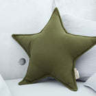 Das Sternkissen Doppelkrepp Grün Herbstgrün von KraftKids, ein grünes sternförmiges Kissen, sitzt vor hellgrauen Kissen auf einem hellen Sofa mit einer Betonwand - ideal, um jedem Kinderzimmer Charme zu verleihen.