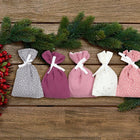 Fünf Adventssäckchen aus Musselin in Rosa, Purpur, Weiß und Grau mit weißen Punkten und Schleifen von KraftKids - liebevoll arrangiert auf Holz mit Tannenzweigen und roten Beeren. Perfekt als Adventskalender!.