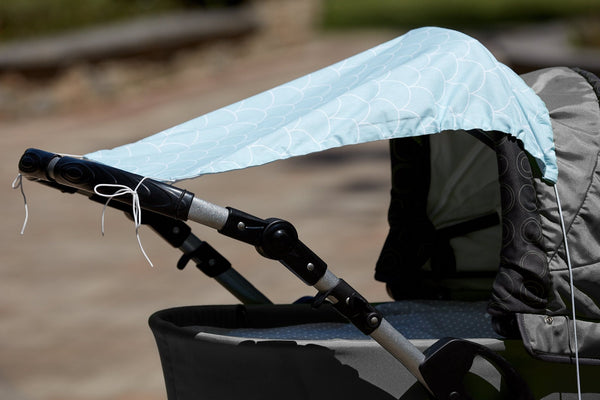 Die Nahaufnahme eines Kinderwagens zeigt das KraftKids Sonnensegel "weiße Halbkreise auf Pastelmint", das über das Verdeck drapiert ist und Ihrem Baby Sonnenschutz bietet. Der Kinderwagen steht an einem sonnigen Tag im Freien, der Hintergrund ist leicht verschwommen.
