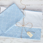 Ein gefaltetes KraftKids Bettwäscheset Uniweiss (weiße Halbkreise auf Pastelblau) aus 100% Baumwolle liegt auf weißem Holz, gebunden mit brauner Schnur und "Kristall" Tag - für erholsamen Schlaf.