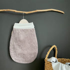 Ein kleiner, grauer Cord-Strampelsack Herbst Winter von KraftKids hängt an einem Holzstab an einer dunklen Wand. Rechts daneben sorgt ein geflochtener Korb mit Henkeln und einem weichen Tuch im Inneren für eine gemütliche, saisonale Atmosphäre.