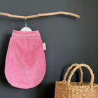 Ein KraftKids Strampelsack Herbst Winter Cord Breitcord Rosa Babyschlafsack hängt an einem hölzernen Ast vor einer schwarzen Wand, mit einem geflochtenen Strohkorb mit Griffen unter dem Ast auf der rechten Seite.