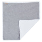 Die KraftKids Wickelunterlage Musselin grau Punkte ist eine rechteckige, graue Babydecke mit weißen Punkten, einem weißen Rand und einem hellbraunen Anhänger. Eine Ecke lässt sich umklappen, so dass die glatte Unterseite zum Vorschein kommt; sie dient auch als praktische Wickelunterlage.