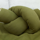 Eine weiche olivgrüne KraftKids Wickeltischumrandung Doppelkrepp Grün Herbstgrün, stilvoll geknotet, ruht auf einer passenden weiß umrandeten Decke, perfekt als Bettrolle Baby oder Kantenschutz Wickelkommode, abgebildet auf hellgrauem Hintergrund.