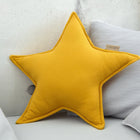 Das Sternkissen Doppelkrepp Gelb Mustard von KraftKids liegt auf hellgrauen Kissen auf einem Sofa vor einer hellen Betonwand - ideal für jedes gemütliche Kinderzimmer.