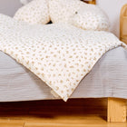 Das KraftKids Bettwäscheset Musselin Zweige braun, handgefertigt aus 100% Baumwolle in Hellgrau mit dezentem Zweigmuster, ergänzt durch Holzbeine, eine Korblampe und einen sanft beleuchteten Holzboden, ist ein hübsches Bett.