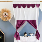 Das KraftKids Puppentheater Kasperletheater Musselin purpur inkl.. Teleskopstange mit weißen und lila Vorhängen vor einer geometrischen Wand, mit einem Jungen und einer Hundepuppe, sowie Strohlöwen-Dekor und einer Kreidetafel in der Nähe.
